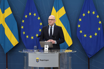 Arbetsmarknadsminister Johan Brtitz står vid ett podie i pressrummet i Rosenbad. I bakgrunden syns svenska flaggan och EU-flaggan.
