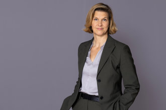 Jämställdhetsminister Nina Larsson står framför en grå vägg och tittar in i kameran.