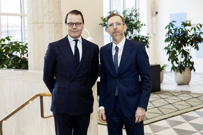 Prins Daniel och socialminister Jakob Forssmed står bredvid varandra i en ljus, modern inomhusmiljö med stora fönster, gröna växter och marmordetaljer.
