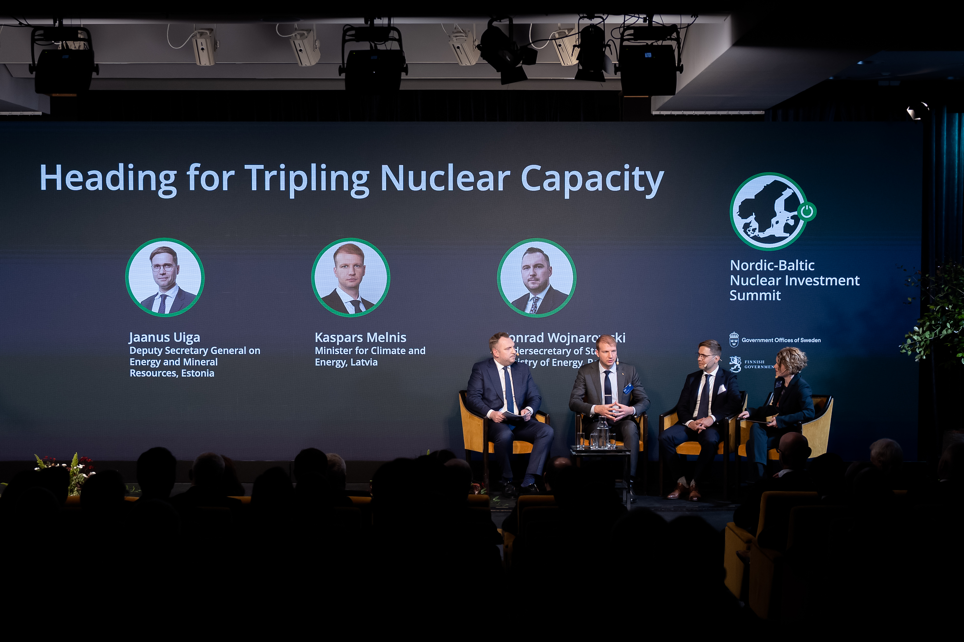 Tre regeringsrepresentanter sitter på scenen i ett samtal som leds av moderatorn Kirsty Hogan