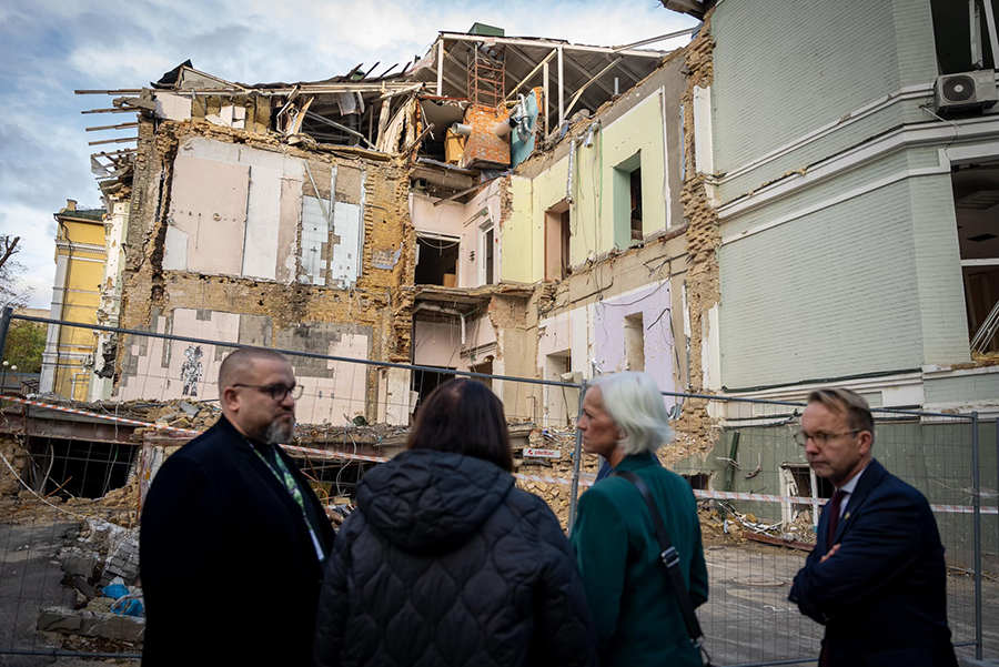 En grupp personer framför en bombad byggnad.