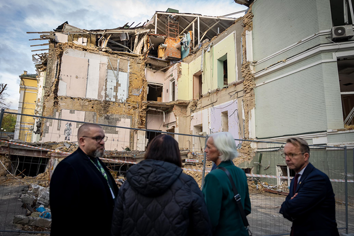 En grupp personer framför en bombad byggnad.