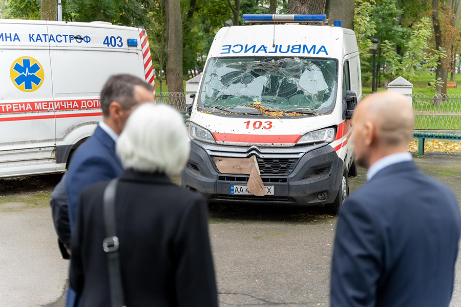 En grupp personer framför en skadad ambulansbil.