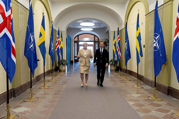 Statsminister Ulf Kristersson och Islands president Halla Tómasdóttir går genom en korridor dekorerad med svenska och isländska flaggor. 