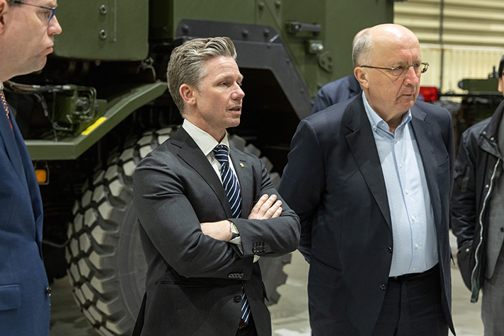 Jonson och Kubilius står och lyssnar på en presentation inne i en monteringshall. I bakgrunden ses sidan av fronten på en Archer. 