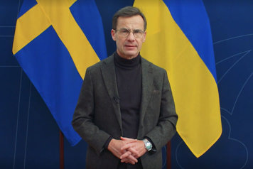 Statsministern talar och tittar in i kameran framför Sveriges och Ukrainas flaggor
