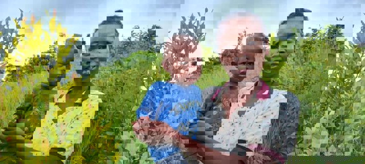 Kvinna med barn i famnen framför växtlighet.