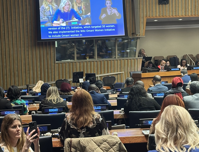 En stor loka med flera sittande personer. På väggen finns en bildskärm som visar jämställdhets- och arbetslivsminister Paulina Brandberg. 