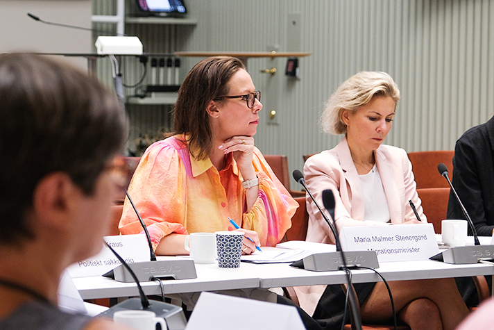 Foto på migrationsminister Maria Malmer Stenergard vid ett konferensbord med en blond kvinna brevid.