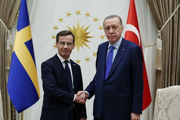 Ulf Kristersson och Recep Tayyip Erdoğan står inomhus och skakar hand framför en svensk och en turkisk flagga