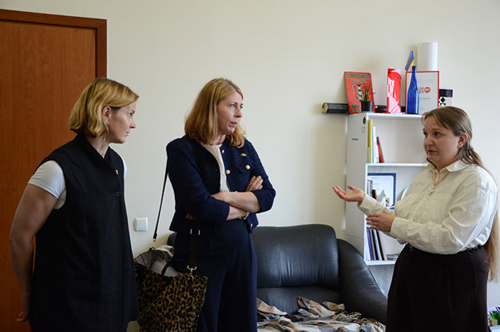 Jämställdhetsminister Nina Larsson och sjukvårdsminister Elisabet Lann står till vänster i bild och tittar mot en kvinna som är placerad till höger.