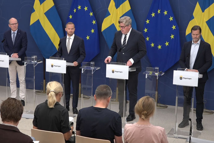 De medverkande står vid var sin talarpulpet framför journalister.