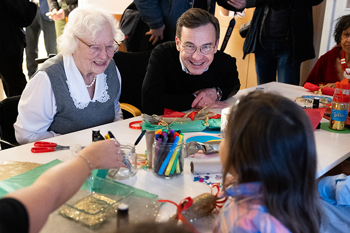 Statsministern sitter med äldre och barn och utför en pysselaktivitet tillsammans.