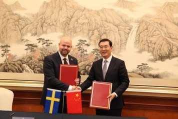 Två män i kostym skakar hand och håller i varsin pärm. I förgrunden visas svenska och kinesiska flaggan.