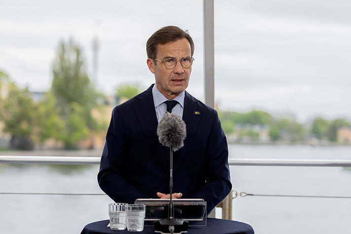 Ulf Kristersson står med ryggen till Strömmen och Skeppsholmen. Framför statsministern står ett bord med en vindskyddad mikrofon.