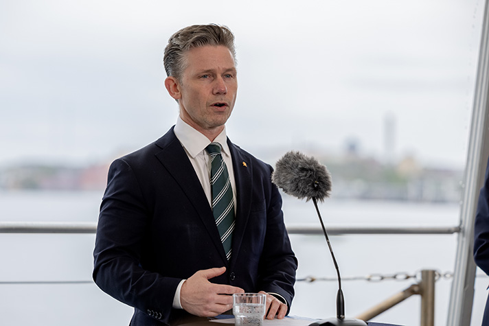 Pål Jonson står med ryggen till Strömmen och Stadsgårdshamnen. Framför försvarsministern står ett ståbord med en vindskyddad mikrofon.