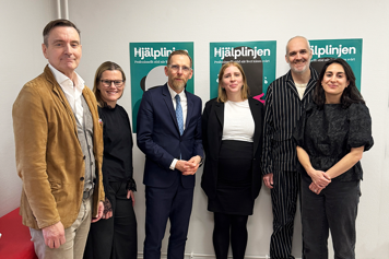 En gruppbild på sex personer. De står framför affischer med texten "Hjälplinjen" på.