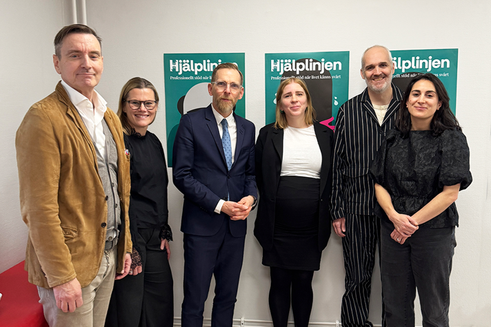 En gruppbild på sex personer. De står framför affischer med texten "Hjälplinjen" på.