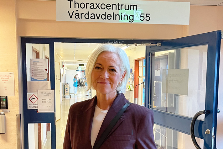 Acko Ankarberg Johansson står framför en dörr på ett sjukhus. Ovanför dörren står det Thoraxcentrum.