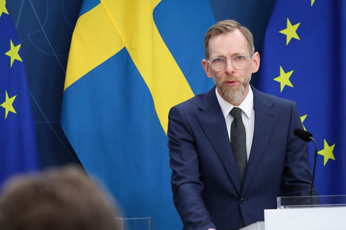 socialminister Jakob Forssmed fotograferad i halvfigur framför fond med flaggor