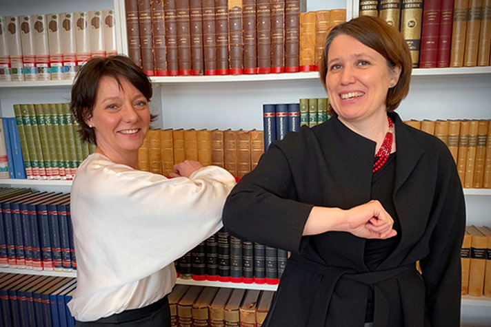 Matilda Ernkrans och Judith Gough hälsa på varandra med armbågarna i ett mötesrum på Utbildningsdepartementet.