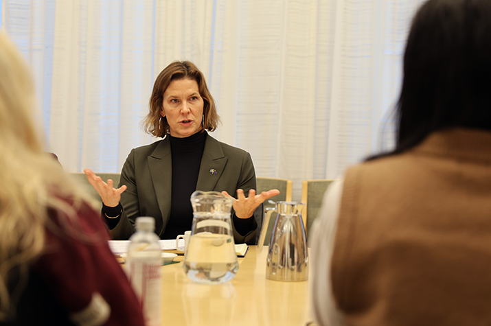 Jämställdhetsminister Nina Larsson sitter vid ett bord och pratar. I förgrunden syns två personer bakifrån.