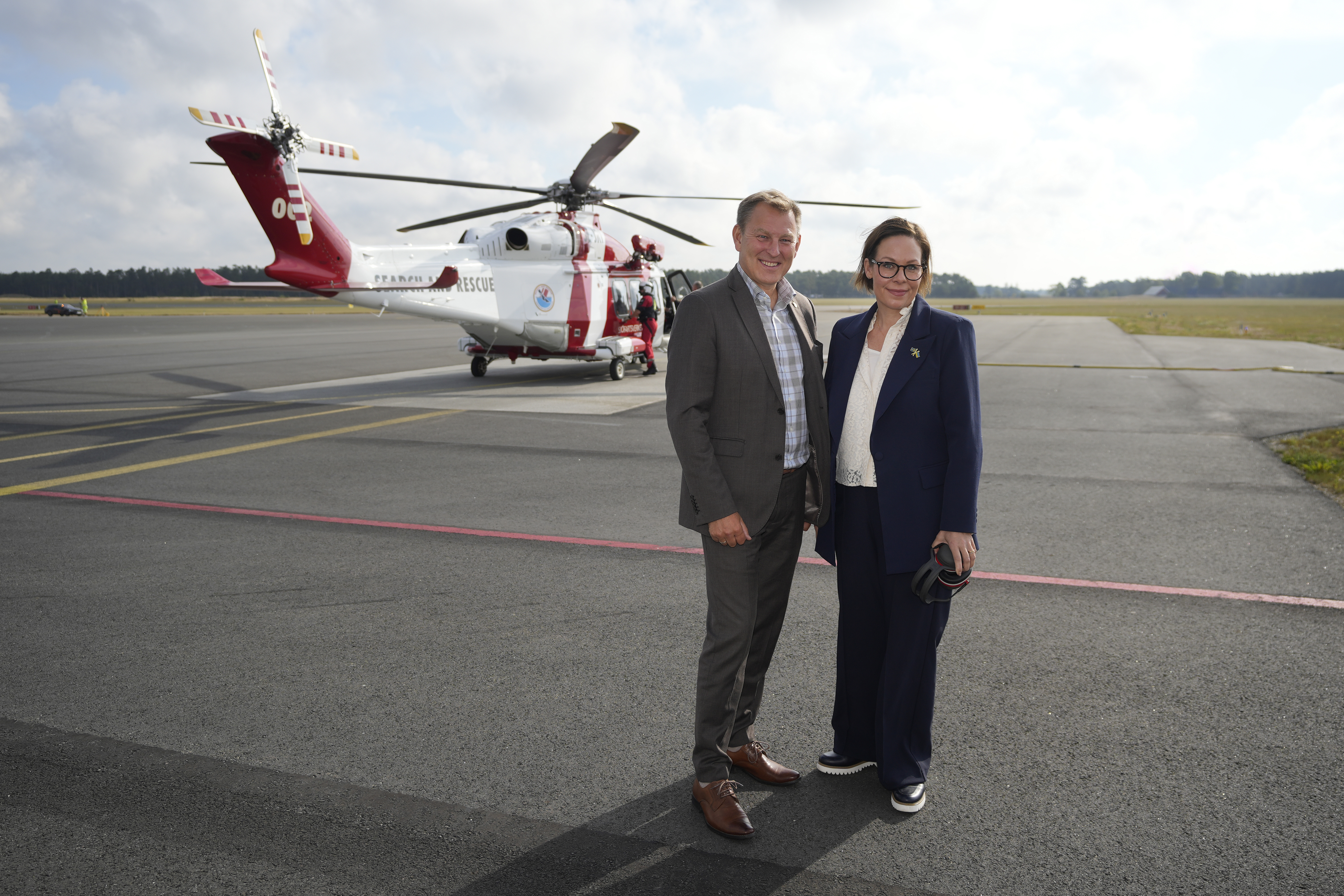 Utrikesministern står bredvid Sjöfartsverkets generaldirektör framför en helikopter.
