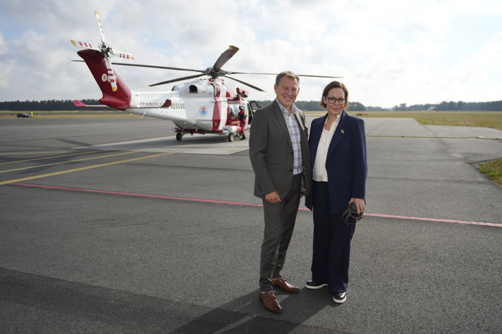Utrikesministern står bredvid Sjöfartsverkets generaldirektör framför en helikopter.