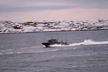 Fartyg med svensk flagga till havs, snötäckt landskap i bakgrunden.