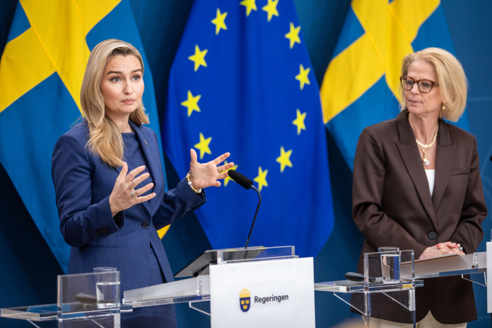 Ebba Busch och Elisabeth Svantesson står vid varsitt podie med flaggor i bakgrunden.