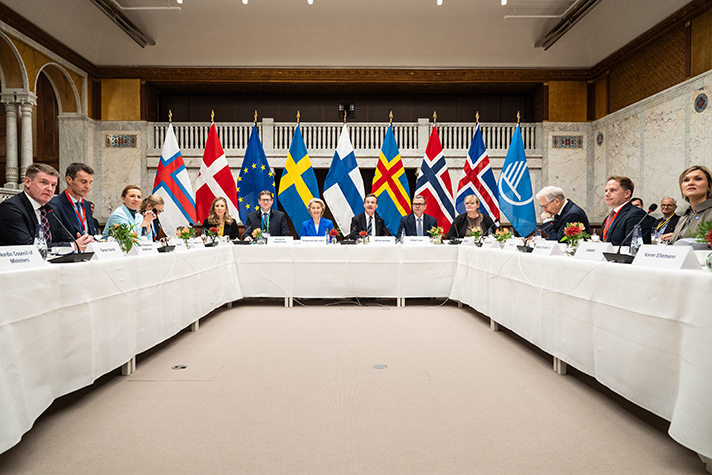 De nordiska statsministrarna och regeringsledarna samt Ursula von der Leyen sitter vid ett hästskoformat bord i ett mötesrum. Bakom dem syns en rad med flaggor: Färöarna, Danmark, EU, Finland, Sverige, Åland, Norge Island, Nordiska rådet.