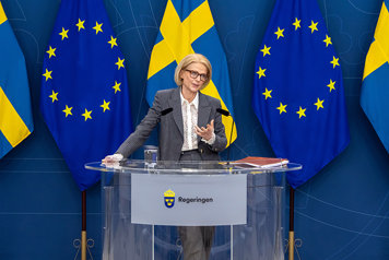 Finansminister Elisabeth Svantesson står vid ett bord på pressträff. I bakgrunden EU-flaggor och svenska flaggor.