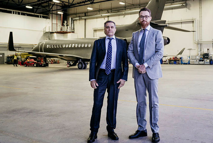Johan Floderus och Saeed Azizi står bredvid varandra i helfigur i en hangar med ett flygplan i fonden.