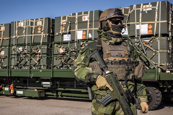 En soldat i uniform står framför en materieltransport.