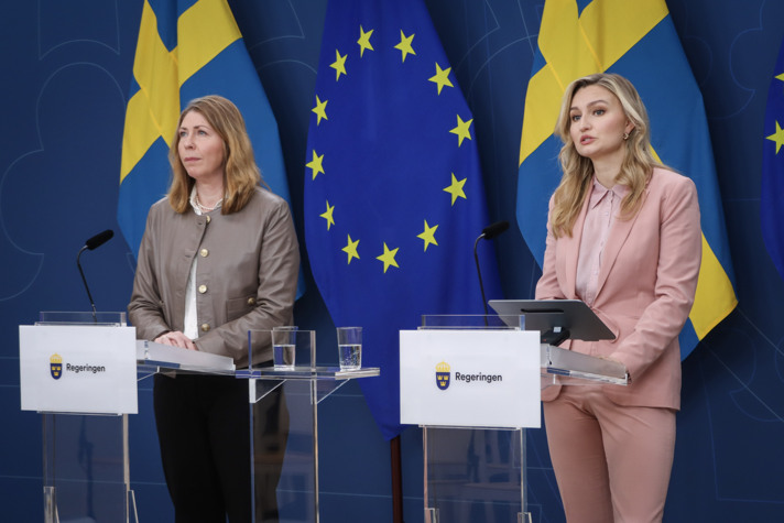 Elisabet Lann och Ebba Busch står och talar vid varsin talarstol i regeringens pressrum. Bakom dem syns den svenska och EU-flaggan.