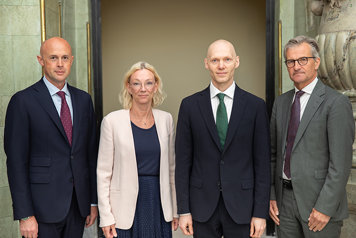 Fyra personer i rad tittar in i kameran. Formellt klädda.