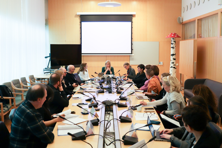 flera personer sitter runt ett sammanträdesbord och pratar.