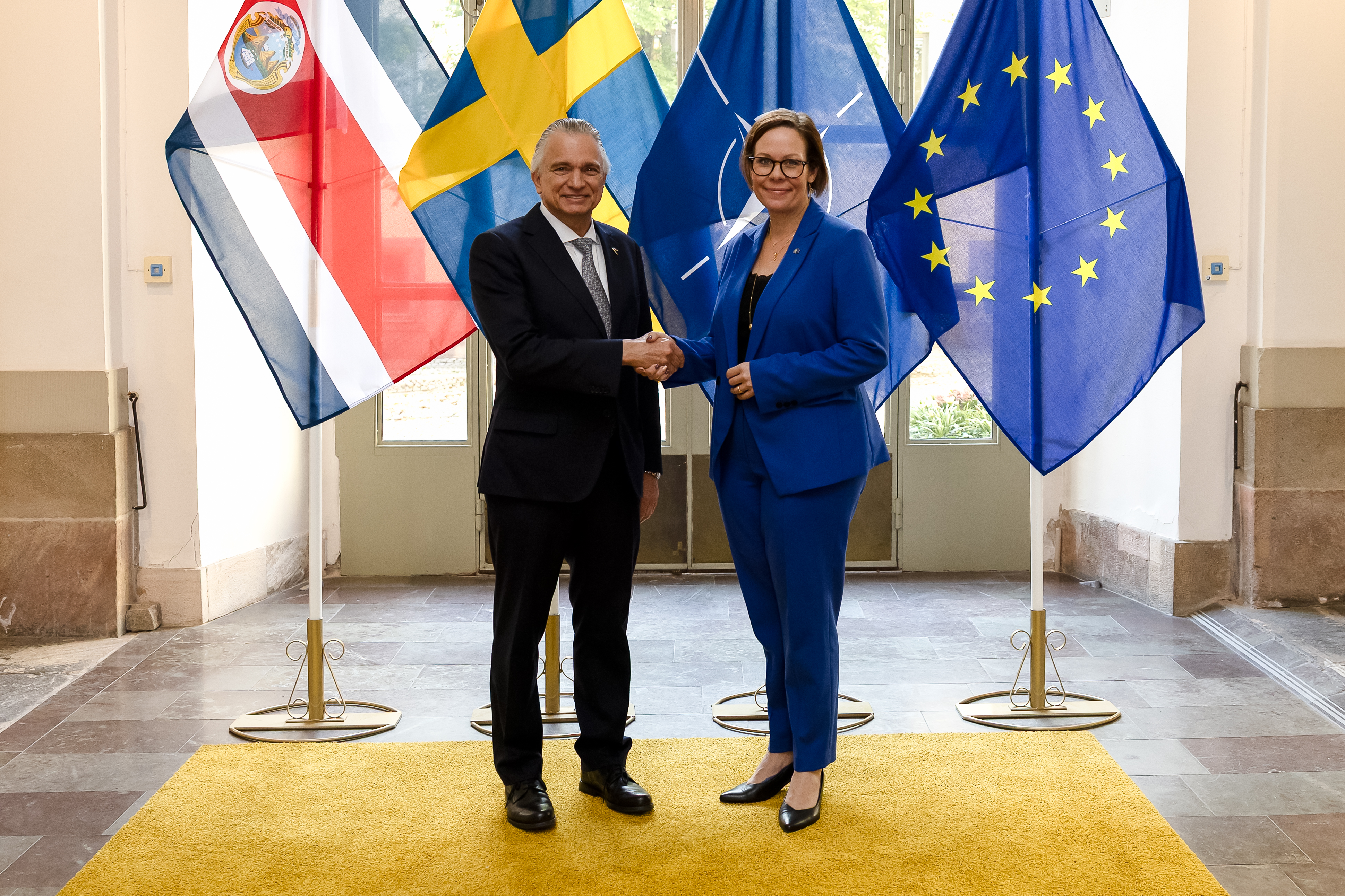 Maria Malmer Stenergard och Arnoldo André Tinoco skakar hand och ser glada ut.
