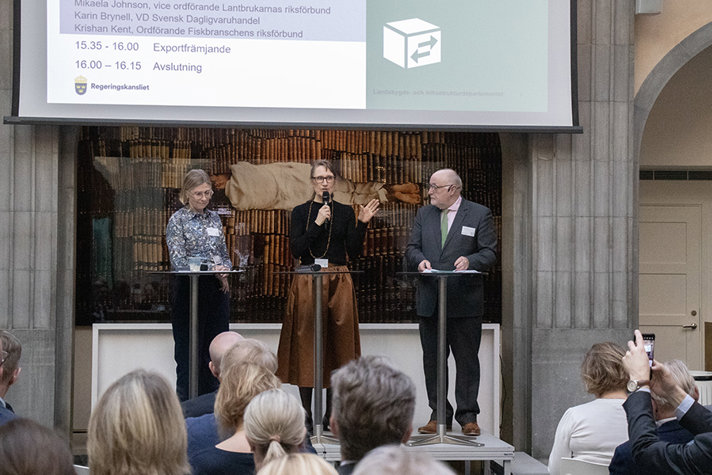 Tre personer står på en scen och pratar framför en publik