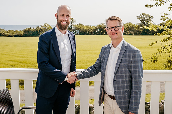 På en solig terrass med utsikt över havet skakar Carl-Oskar Bohlin och Torsten Schack Pedersen hand efter påskriven avsiktsförklaring