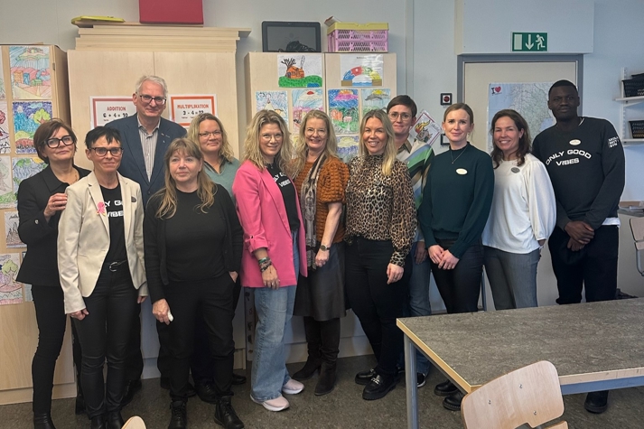Personal på Andersbergsskolan och projektet "Skolan mitt i byn" tillsammans med skolministern står i ett klassrum.