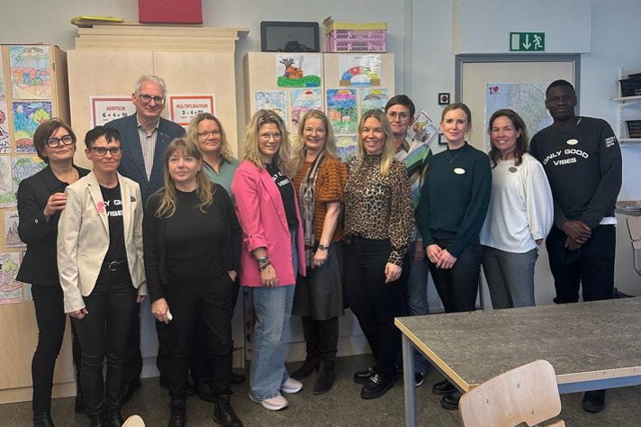 Personal på Andersbergsskolan och projektet "Skolan mitt i byn" tillsammans med skolministern står i ett klassrum.