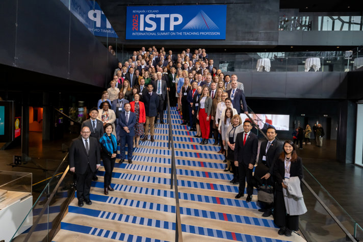 En stor grupp delegater från olika länder står på en bred trappa under en banderoll där det står "ISTP 2025: International Summit on the Teaching Profession".