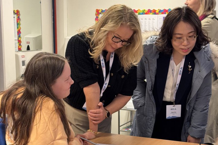 Ett barn sitter vid en skolbänk och pratar med skolministern och en till kvinna ur delegationen.