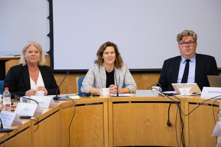 Tre personer sitter bredvid varandra vid ett stort mötesbord.