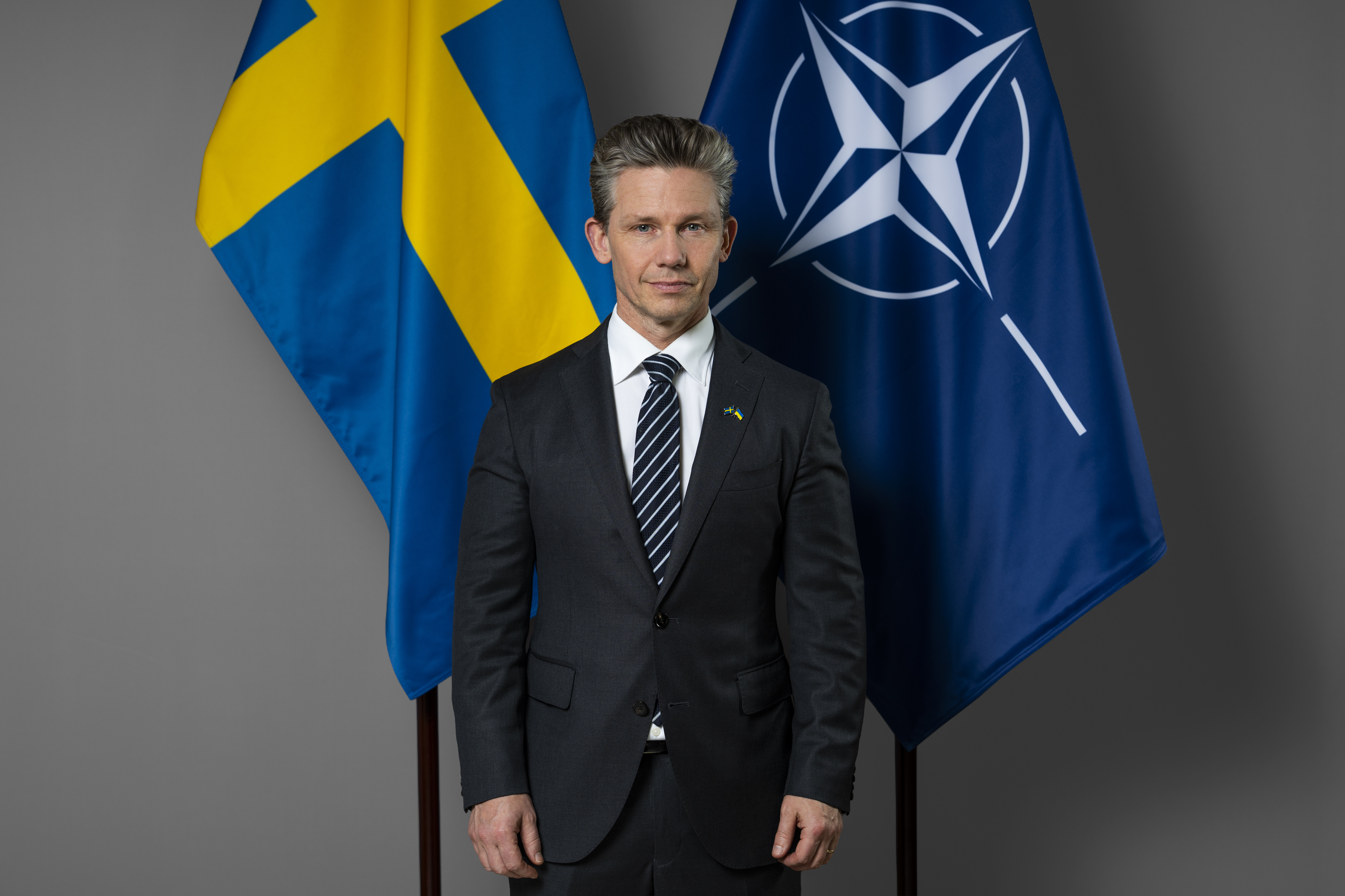 Porträtt på Pål Jonson med svenska flaggan och Natos flagga i bakgrunden