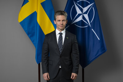 Porträtt på Pål Jonson med svenska flaggan och Natos flagga i bakgrunden