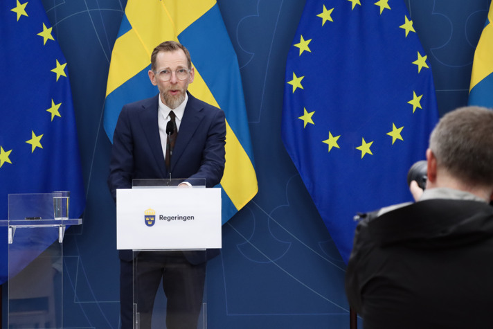 Jakob Forssmed står vid en talarstol, framför svenska och EU-flaggan, i regeringens pressrum.
