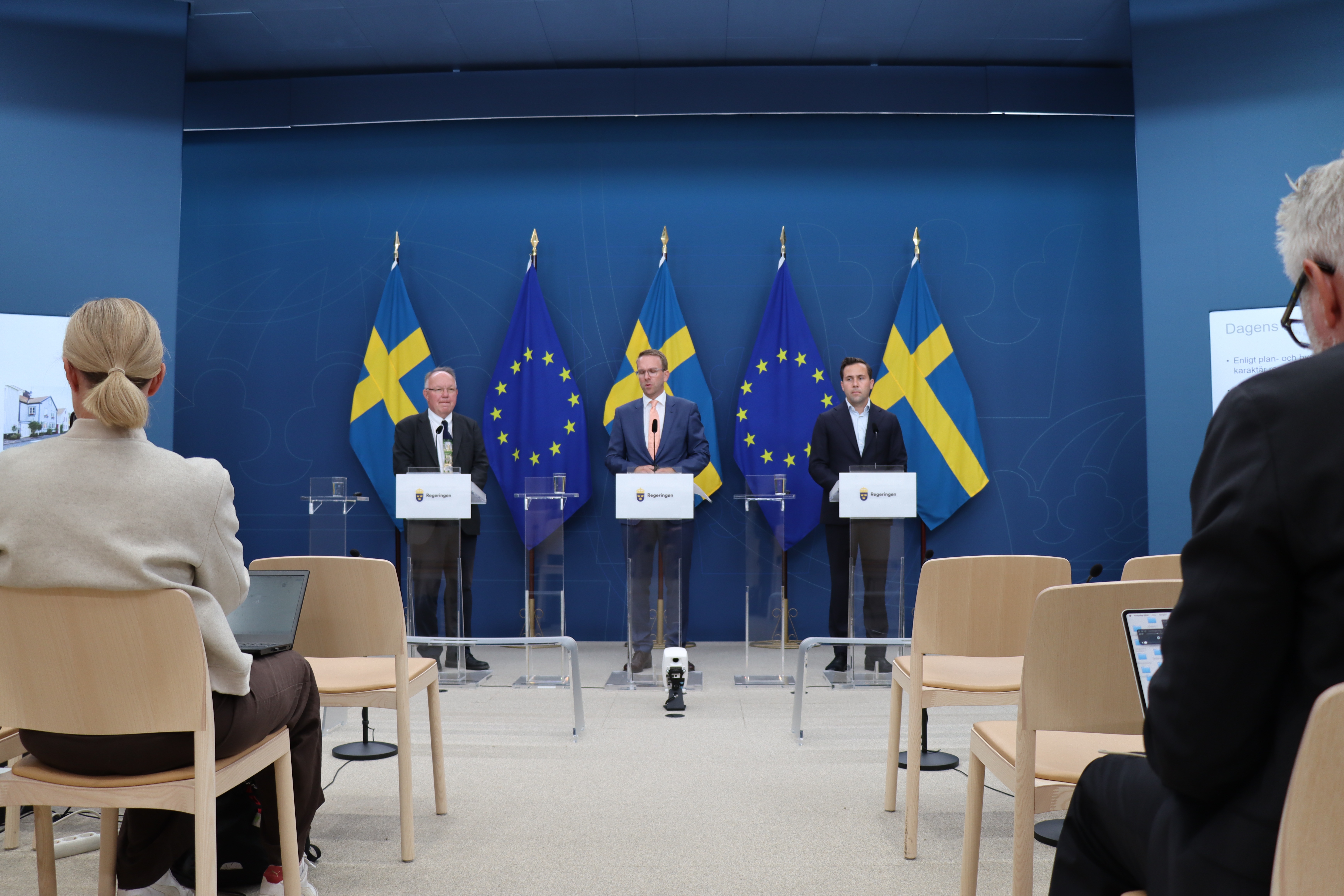 tre representanter för regeringen talar på en pressträff