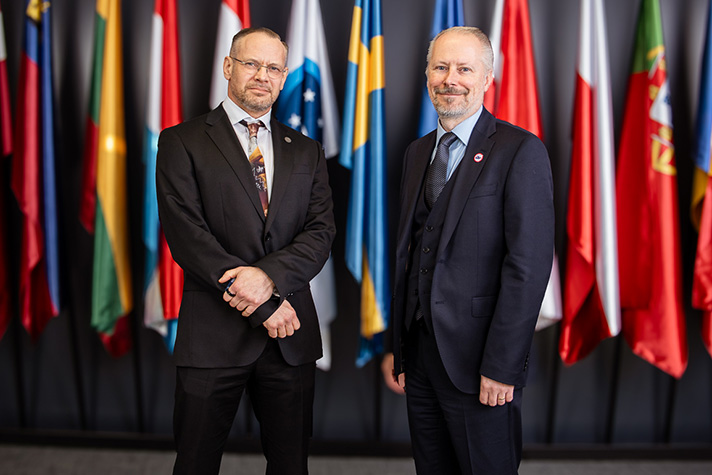  Statssekreterare Anders Hall och Lars Gerdes, biträdande verkställande direktör för den operativa verksamheten framför flera flaggor.